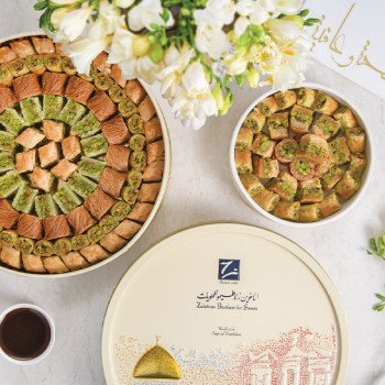 مشكل بقلاوة من الأخوين زلاطيمو بتشكيلة الأقصى وتغليف فاخر مزخرف بالأبيض والذهبي مع ورود بيضاء